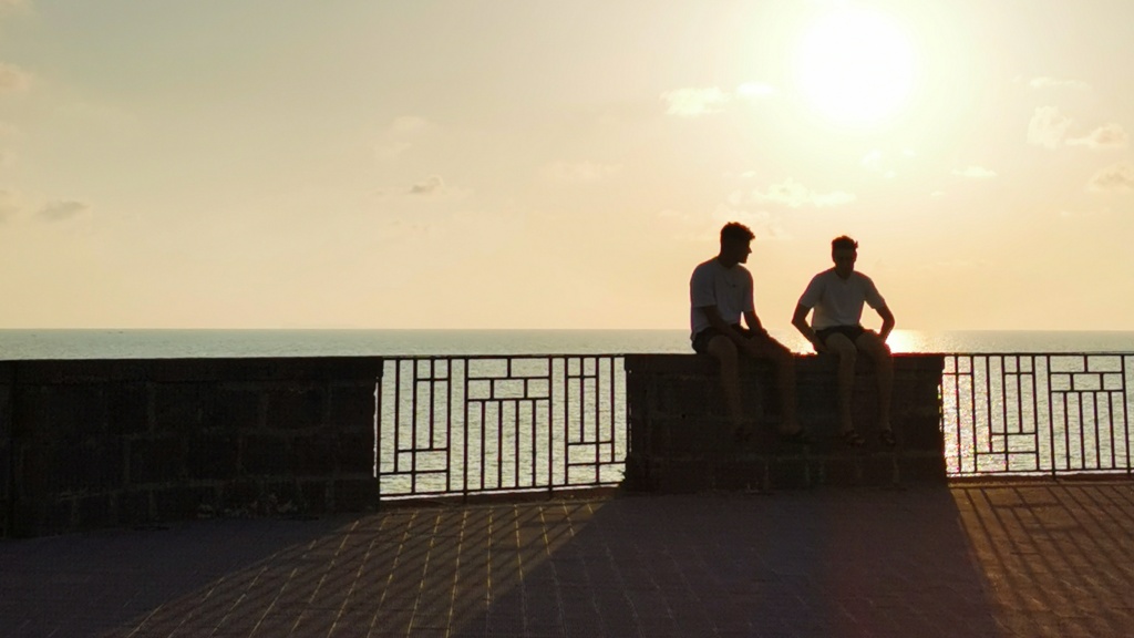 2 boys sitting on a wall as the sun goes down